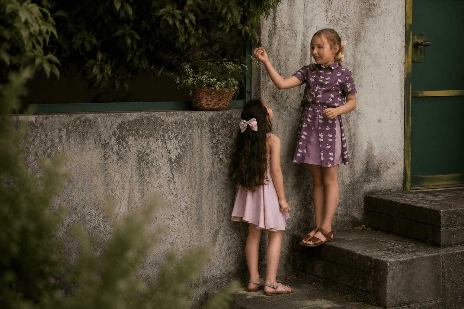 Two Farway Milano girls in summer dresses beside a low stone wall