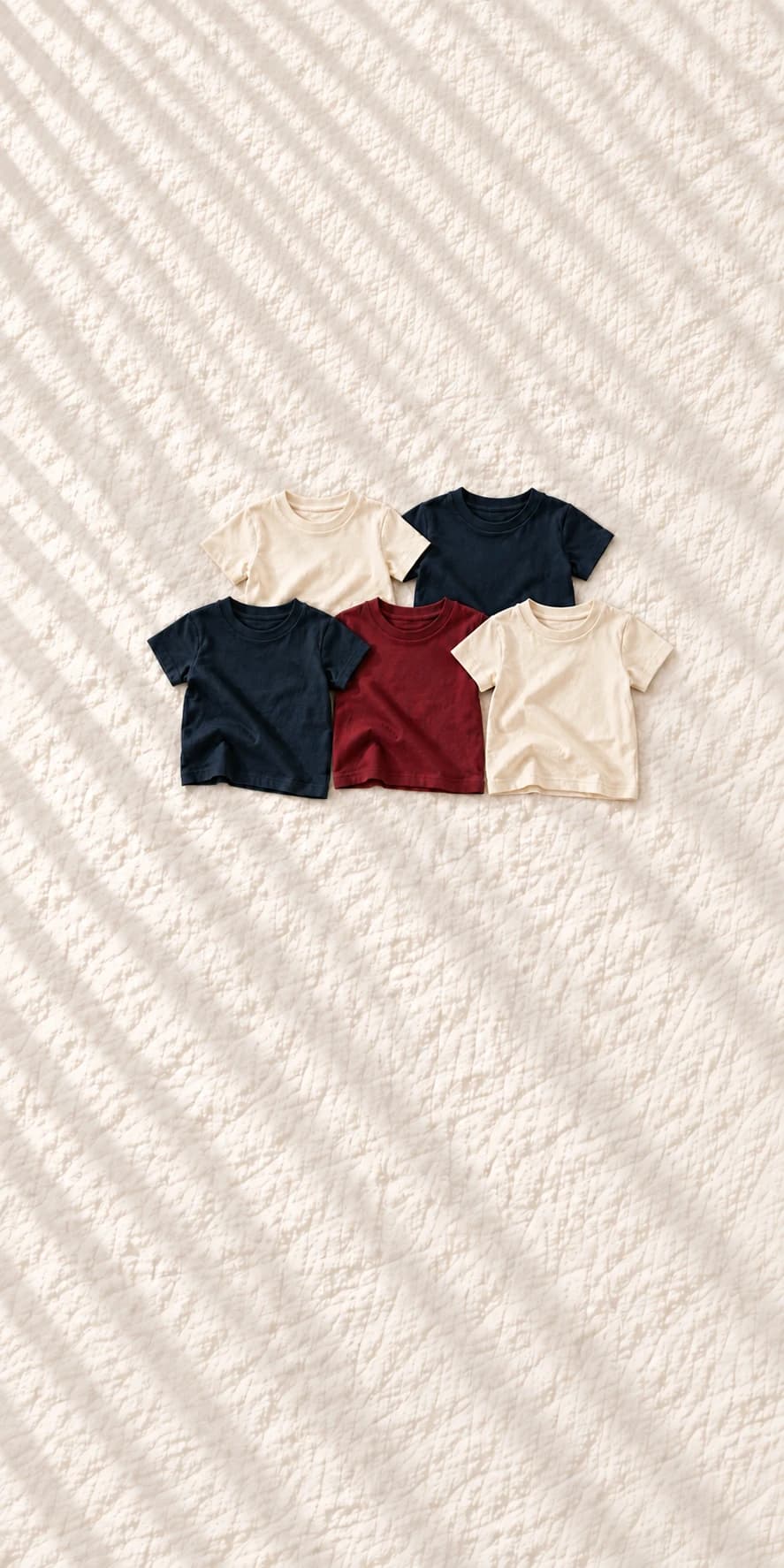 Five Farway kids T-shirts in ivory, navy and burgundy, arranged on light linen
